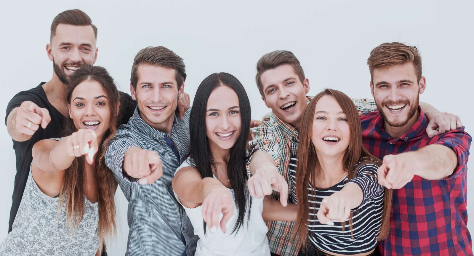 Sieben junge Menschen stehen nebeneinander und zeigen lachend in die Kamera