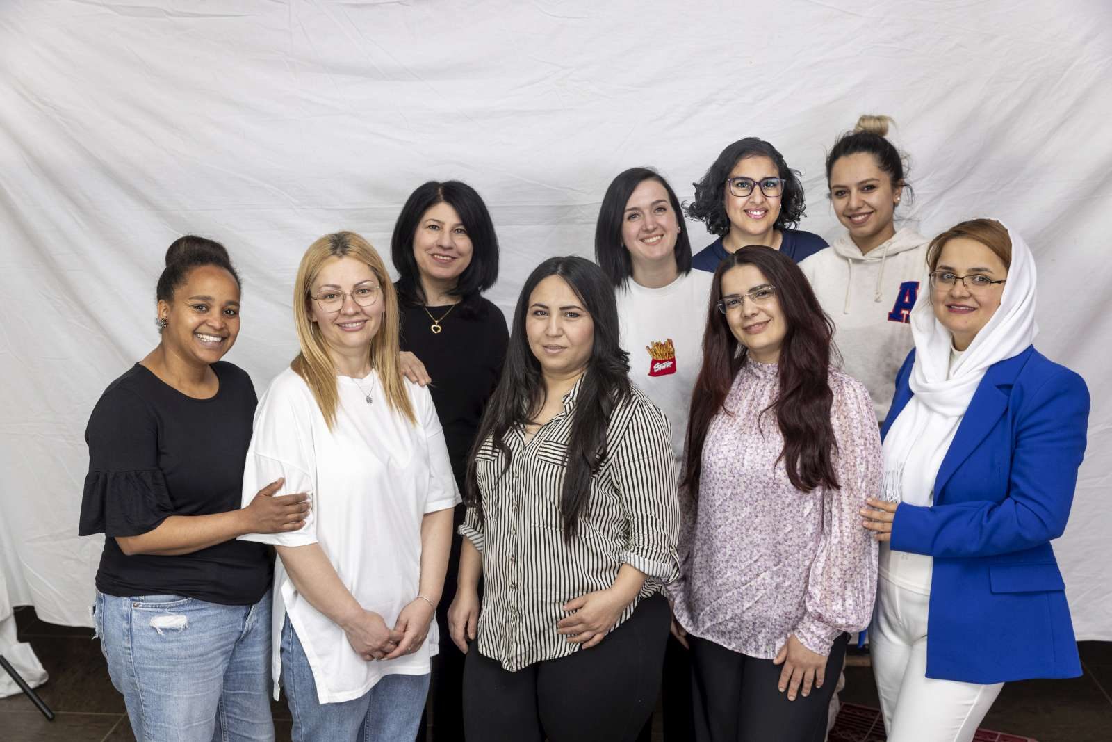 Zehn Frauen stehen vor einem hellen Tuch und blicken in die Kamera