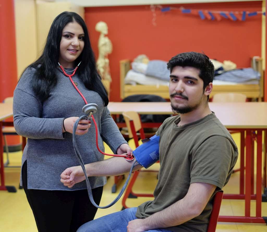 Zwei Lernende üben das Blutdruckmessen in einem Pflegeraum