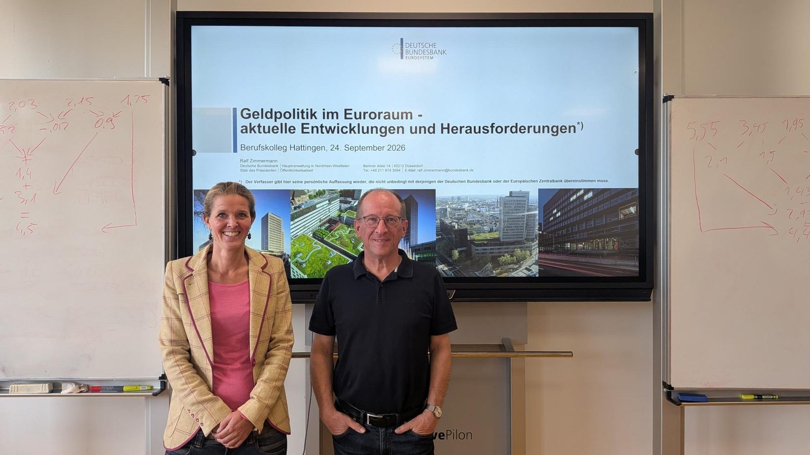 Ralf Zimmermann von der Deutschen Bundesbank und eine Lehrerin vor dem Bildschirm mit der Titelfolie „Geldpolitik im Euroraum – aktuelle Entwicklungen und Herausforderungen“