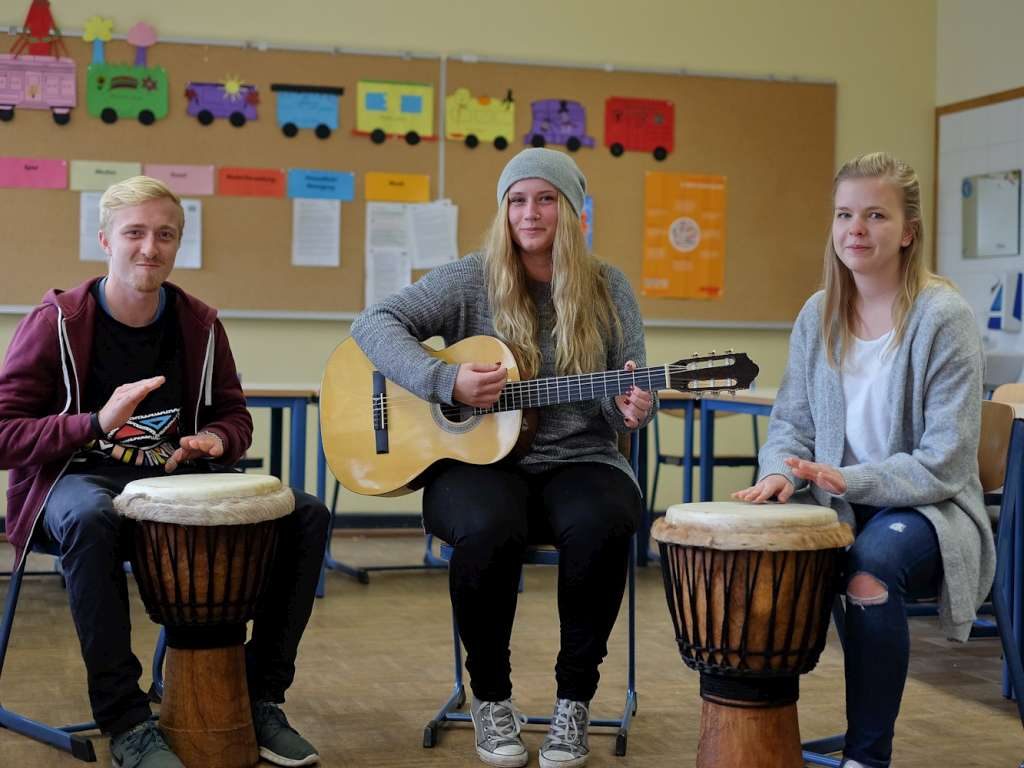Lernende musizieren mit Trommeln und Gitarre in einem Klassenraum