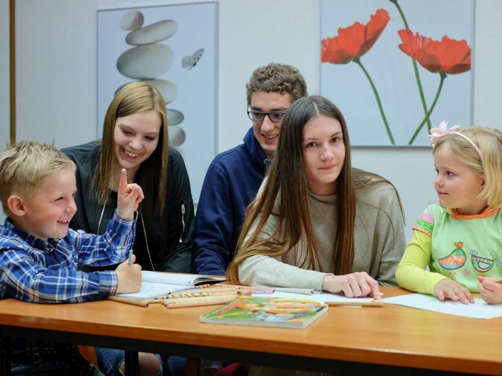 Lernende sitzen mit zwei Kindern an einem Tisch und spielen