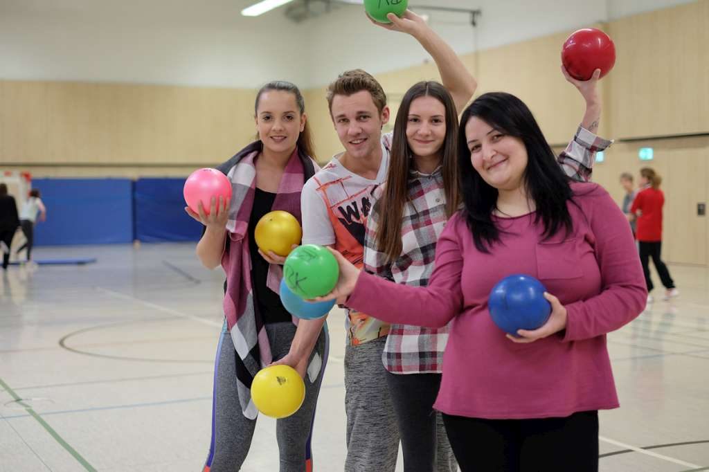 Lernende halten bunte Bälle in einer Turnhalle