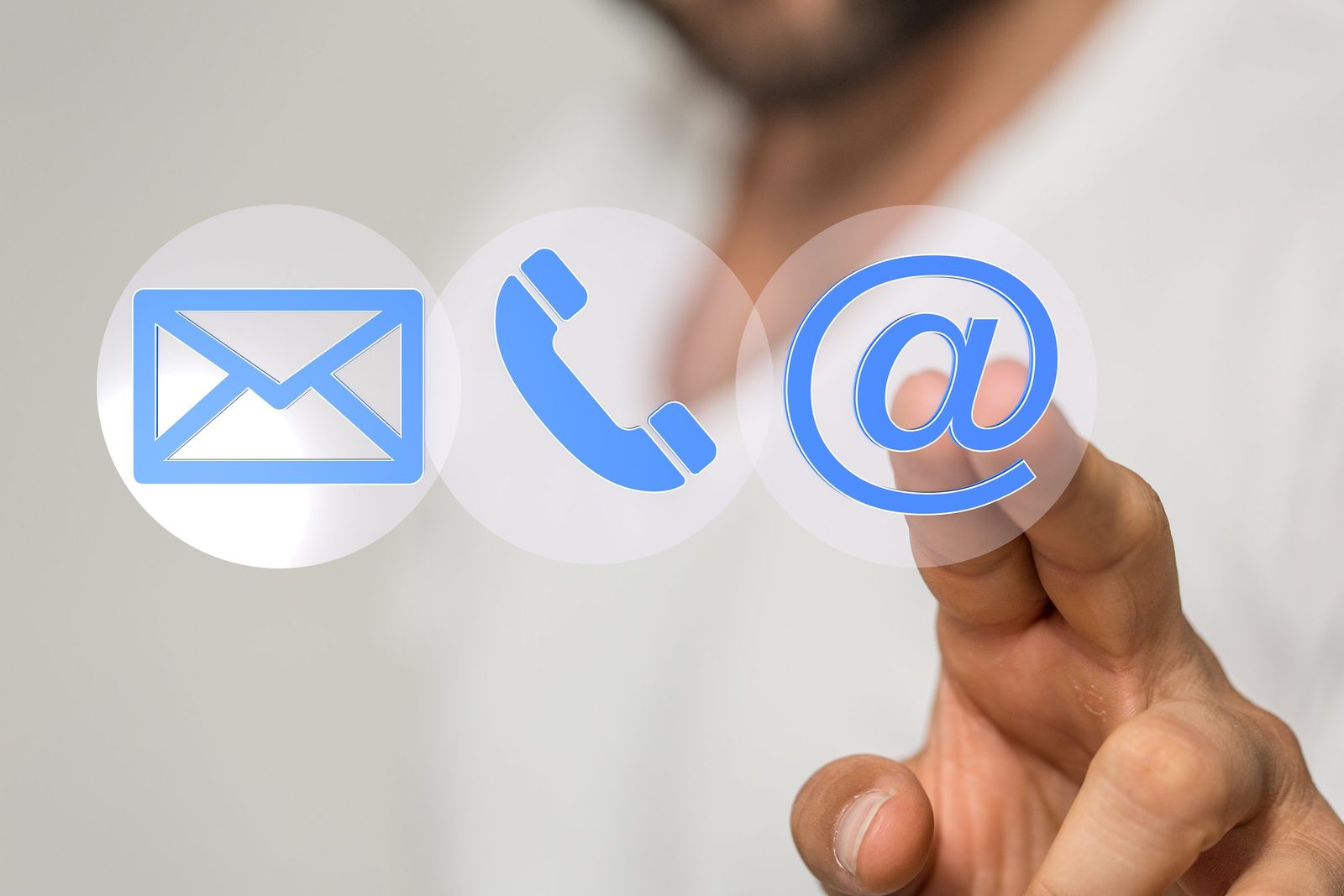 Ein Finger tippt auf drei schwebende Symbole für Brief, Telefon und E-Mail