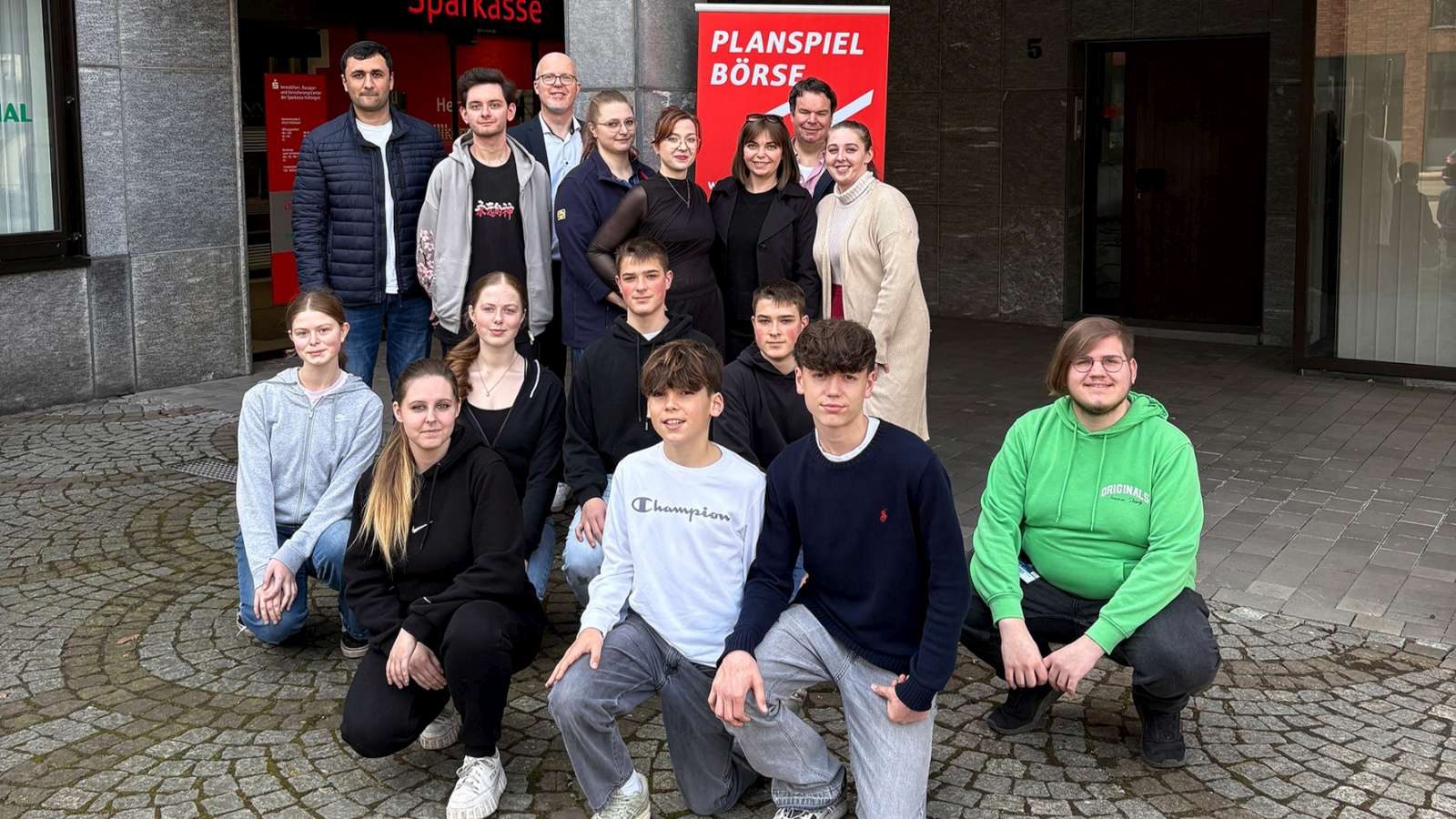 Lernendengruppe vor einem Rollbanner zum Planspiel Börse
