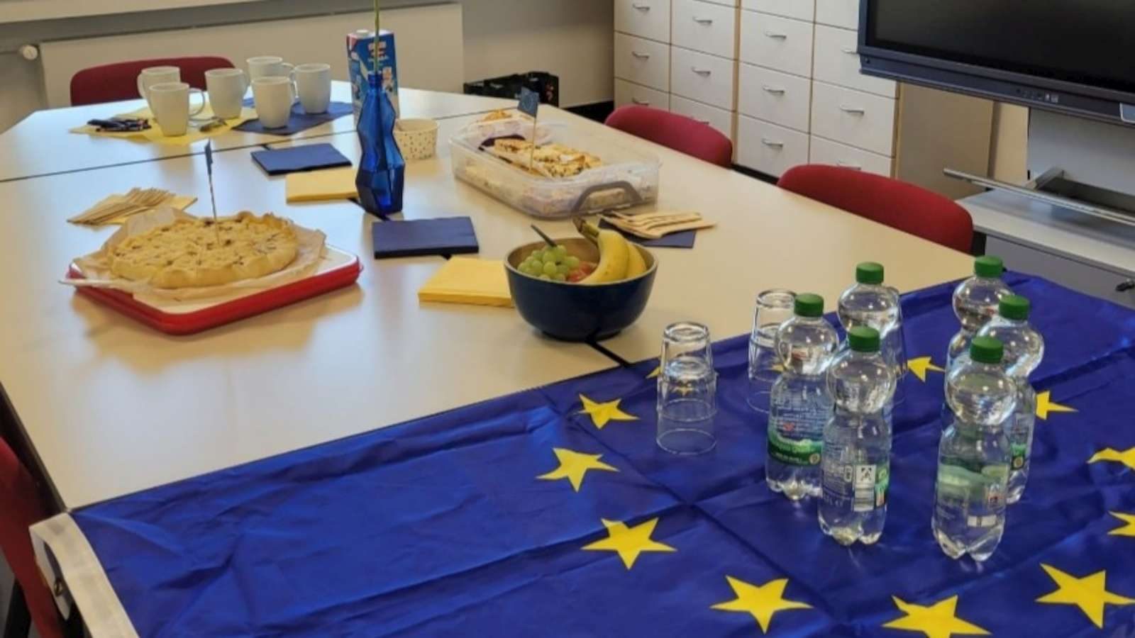 Gedeckter Besprechungstisch mit Kuchen, Obst und Getränken auf einer Europaflagge