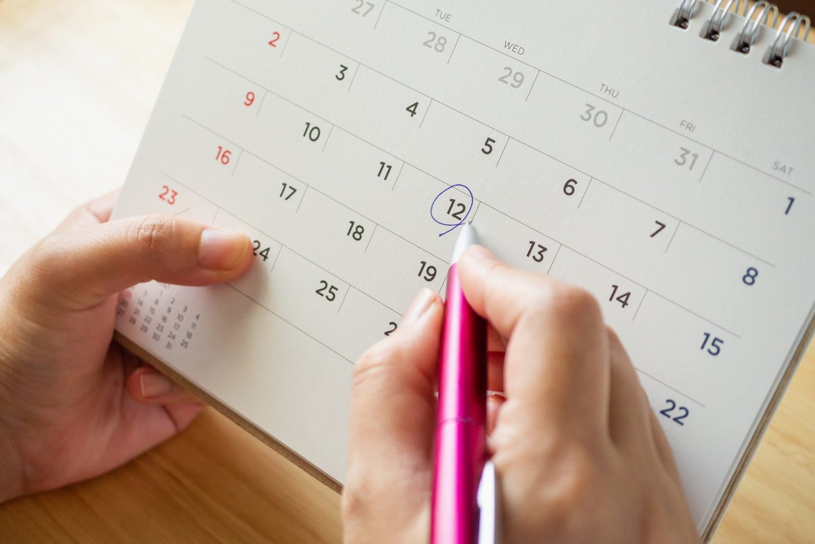 Eine Hand kreist mit einem Stift ein Datum in einem Tischkalender ein