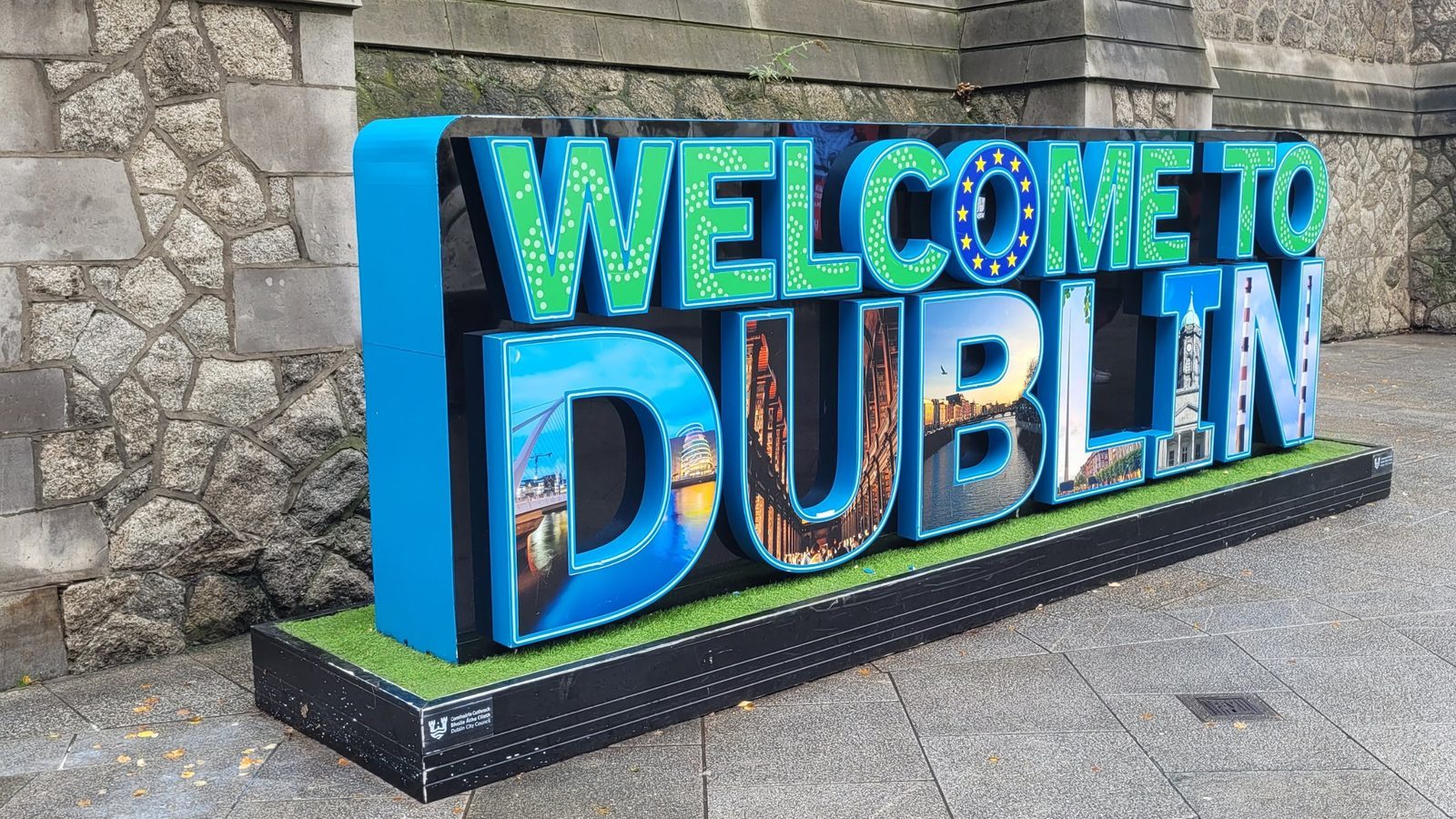 Bunter Schriftzug „Welcome to Dublin“ vor einer Steinmauer, in den Buchstaben Fotos von Sehenswürdigkeiten der Stadt