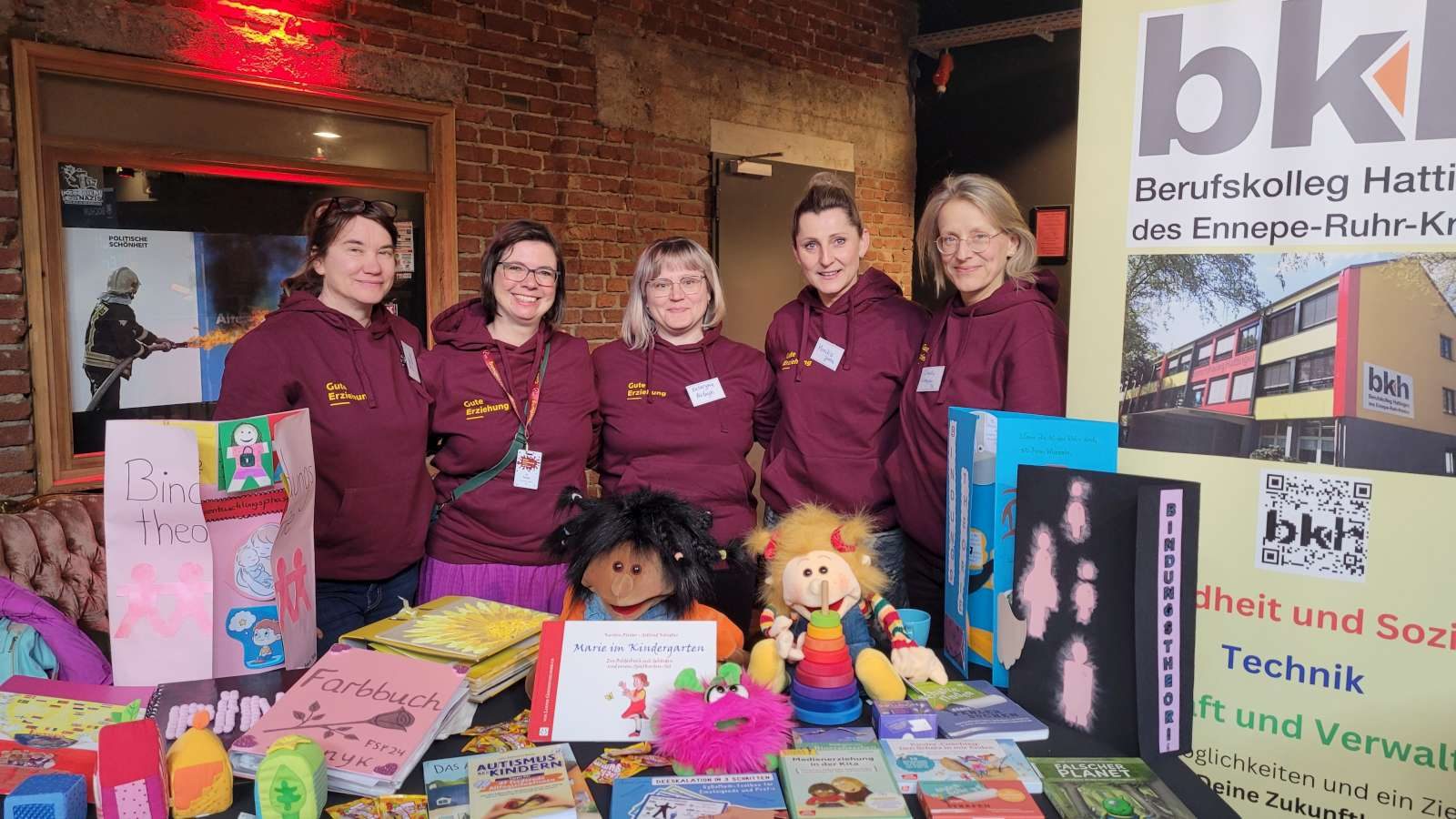 Fünf Lehrerinnen stehen an einem Messestand des Berufskollegs mit Bilderbüchern und Spielmaterial