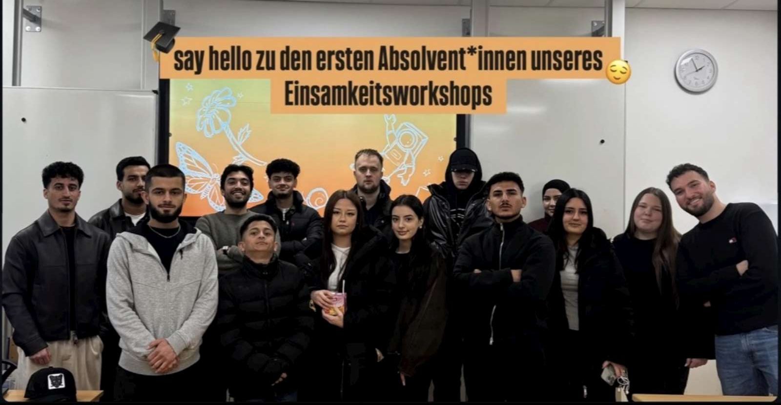 Teilnehmende stehen vor einer Leinwand mit dem Gruß an die ersten Absolventinnen und Absolventen des Einsamkeitsworkshops